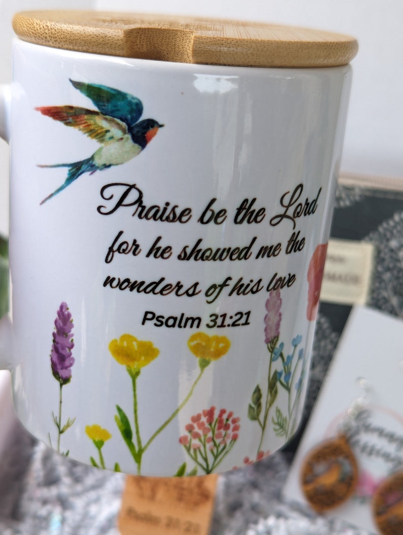Pu&ograve; includere: Tazza in ceramica bianca con coperchio in bamb&ugrave;. La tazza presenta un design di uccello colorato e il testo "Lodato sia il Signore perch&eacute; mi ha mostrato le meraviglie del suo amore Salmo 31:21".