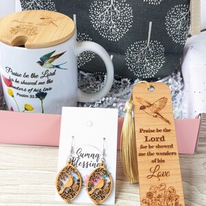 Pu&ograve; includere: Una scatola regalo piena di articoli a tema religioso. La scatola contiene una tazza con un design di uccello e fiori, un segnalibro con un design di uccello e fiori, un paio di orecchini in legno con un design di uccello e fiori e una piccola borsa di stoffa grigia e bianca con motivo.