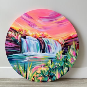 Pode incluir: Pintura redonda de uma vibrante cena de cachoeira. A obra apresenta um céu de pôr do sol colorido com tons de rosa, laranja e roxo. A cachoeira cai em uma piscina, cercada por folhagens exuberantes verdes e rosas.