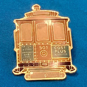 May include: A gold-toned metal enamel pin shaped like a cable car. The design features a brown body with gold outlines, the number 501, and the text COST PLUS printed in white on a dark green background. The pin has a classic trolley silhouette.