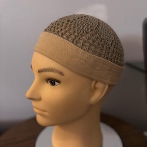 May include: A tan crocheted skullcap with a wide elastic band. The skullcap has a mesh design and is worn on a mannequin head.