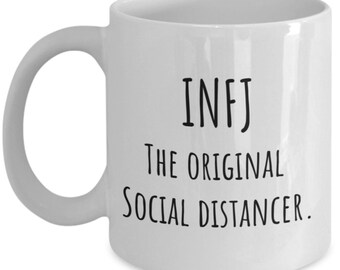 May include: White ceramic coffee mug with black text that reads "INFJ The Original Social Distancer."