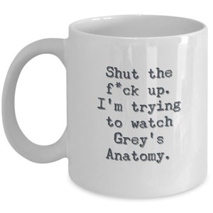 May include: White ceramic mug with a curved handle. The mug features black text that reads: "Shut the f*ck up. I'm trying to watch Grey's Anatomy."