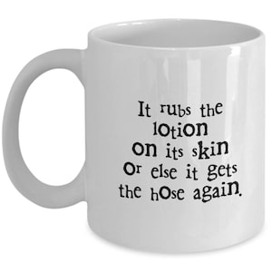 May include: White ceramic mug with a curved handle. The mug features black text that reads, "It rubs the lotion on its skin Or else it gets the hose again."