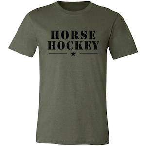 May include: An olive green short-sleeved t-shirt featuring the black text HORSE HOCKEY printed in a distressed, stencil-style font across the chest, with a small black star centered between two horizontal lines positioned below the text.