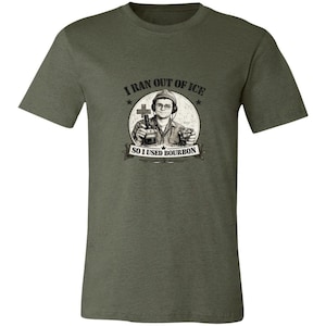 May include: An olive green short-sleeve t-shirt featuring a graphic print of a person wearing a hat and headphones, holding a bottle and a glass. The text reads, I RAN OUT OF ICE SO I USED BOURBON, arranged in a circular design with a cross symbol.