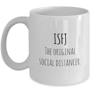 Puede incluir: Taza de café de cerámica blanca con texto negro que dice "ISFJ The Original Social Distancer."