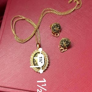 May include: A gold chain necklace with a pendant featuring a black and white enamel design. The pendant is oval shaped and measures 1 1/2 inches in length. The necklace also includes a pair of matching earrings with the same design. The earrings are also 1 1/2 inches in length.