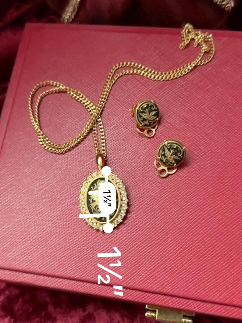 May include: A gold chain necklace with a pendant featuring a black and white enamel design. The pendant is oval shaped and measures 1 1/2 inches in length. The necklace also includes a pair of matching earrings with the same design. The earrings are also 1 1/2 inches in length.