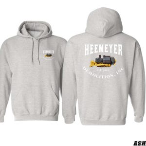 May include: Gray hooded sweatshirt with a white graphic of a yellow bulldozer with the text "Heemeyer Demolition, Inc. Est. 2001" on the back and a smaller version of the graphic on the front.