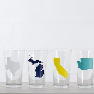 May include: Four clear glass tumblers with state outlines in different colors. The states are Texas, Michigan, California, and Washington.