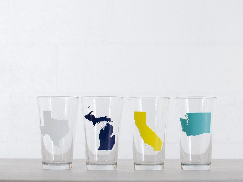 May include: Four clear glass tumblers with state outlines in different colors. The states are Texas, Michigan, California, and Washington.