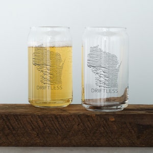 May include: Two clear glass drinking glasses with a black and white outline of the state of Wisconsin. The glasses have the word "Driftless" printed on the bottom.