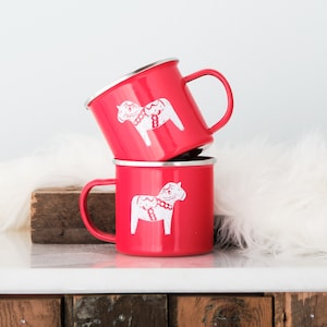 May include: Two red enamel mugs with white Dala horse designs. The mugs have a white rim and handle.