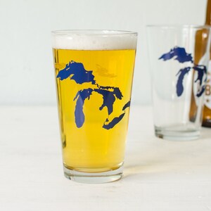 May include: A pint glass with a blue outline of the Great Lakes on the side. The glass is filled with a light-colored beer.