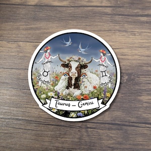 May include: A round sticker featuring a brown and white cow adorned with flowers and a rainbow, set in a field of wildflowers. Two figures flank the cow, and two birds fly above. The text "Taurus - Gemini" is on a banner.