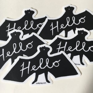 May include: Five black bat stickers with white outlines and the word "Hello" written in white cursive on each. The stickers are on a white surface.