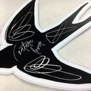 May include: Black and white sticker of a stylized bird with the text "nature lover" written in white on the bird's body.