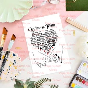 May include: A white greeting card with the text "We're a Team" and a poem about love. The card features a line drawing of two hands holding pinky fingers. The card is surrounded by art supplies and decorative elements.
