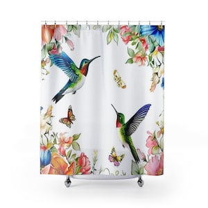 May include: White shower curtain featuring watercolor illustrations of hummingbirds and butterflies amidst colorful flowers. The design includes red, pink, orange, and blue blooms, with green foliage. The hummingbirds have vibrant green, blue, and red plumage.