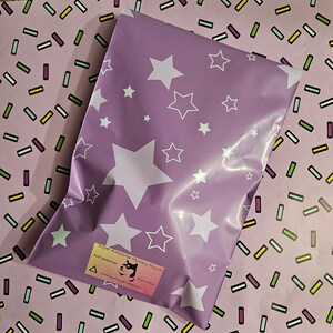 May include: A purple poly mailer with a white star pattern. The mailer has a sticker that says "Super Awesome Mystery Pouch!" with a cartoon dog and the text "Such awesome! Much Wow!" and a website address.