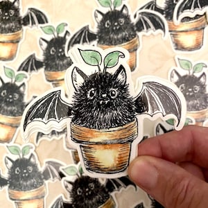 May include: A black bat with green leaves growing from its head is potted in a brown pot. The bat has large wings and is depicted in a cartoon style.