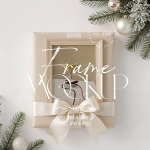May include: A beige frame mockup with a champagne glass inside, tied with a cream ribbon and bow. The image includes text that says "Frame Mockup" and "ISO DIN A RATIO PSD, JPG & PNG". Decorative Christmas ornaments and pine branches are in the background.