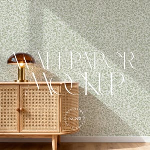 May include: A mid-century modern style cabinet with a woven rattan front and wooden legs. A brass desk lamp with a brown glass shade sits on top of the cabinet. The background is a light green wallpaper with a leaf pattern.