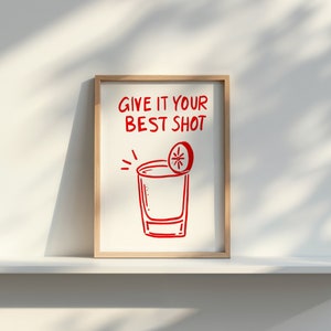May include: A white framed print with red text that says "Give it your best shot" and a red illustration of a shot glass with a lime wedge on top.