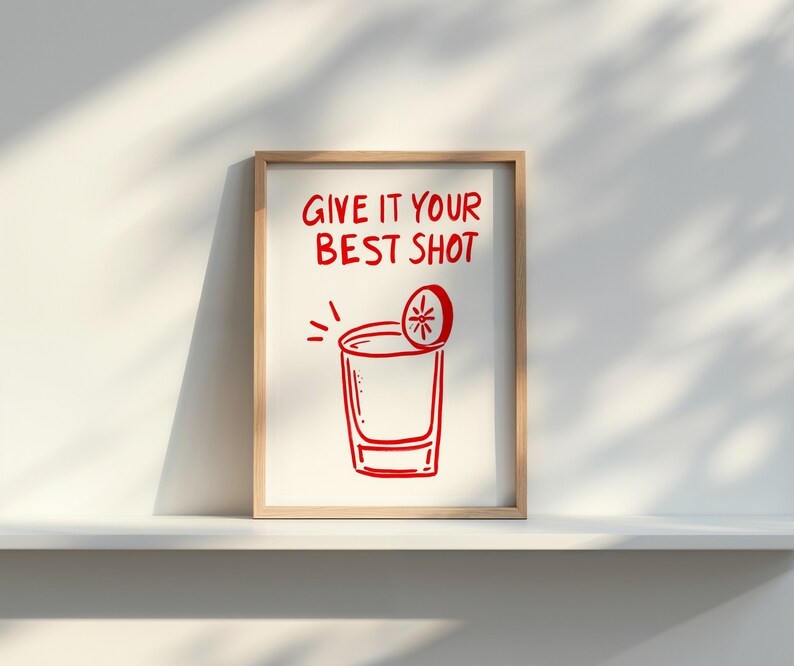 May include: A white framed print with red text that says "Give it your best shot" and a red illustration of a shot glass with a lime wedge on top.