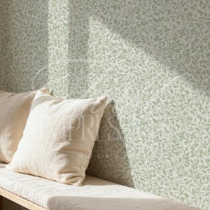 May include: A light-colored bench with two cream-colored pillows. The wall behind the bench is covered in a green and white floral wallpaper pattern. The wallpaper has a repeating design of leaves and vines.