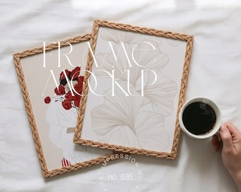 May include: Two rectangular picture frames with woven brown borders. One frame displays a floral illustration with red roses, the other a beige botanical print. A white coffee cup with black coffee sits next to the frames. The text "FRAME MOCKUP" is visible.