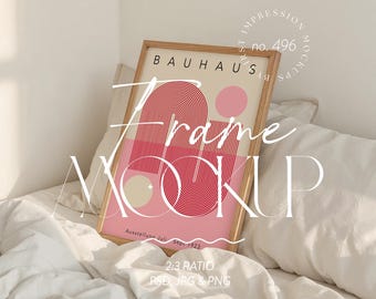 Op de afbeelding: Een ingelijste poster met een minimalistisch ontwerp met het woord "BAUHAUS" en de tekst "Ausstellunn Juli Sept 1923". De poster heeft een roze en rood kleurenschema en wordt weergegeven in een licht houten frame. De woorden "Frame Mockup" staan over de afbeelding.