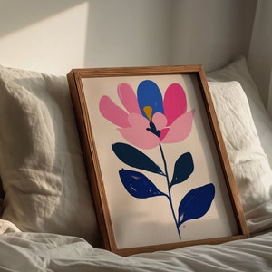 May include: A framed print of a stylized pink, blue, and white flower with green leaves on a white background.