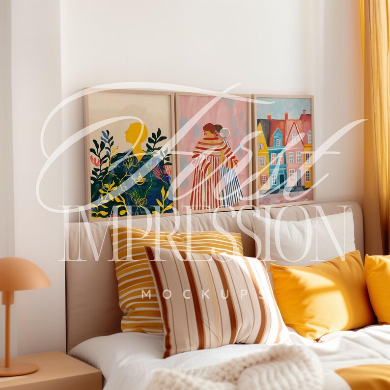 May include: Three framed illustrations on a white wall above a bed with white bedding, yellow and brown striped pillows, and a yellow throw pillow. The illustrations are of a woman in a garden, two women in striped dresses, and a colorful house.