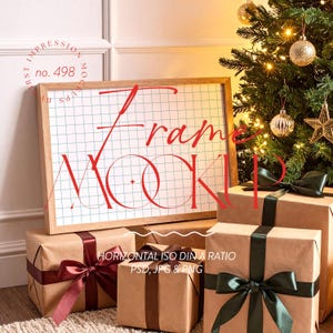 Puede incluir: Una maqueta de marco de madera con un fondo de cuadrícula y la palabra "Frame Mockup" en rojo. Varios regalos envueltos con cintas verde oscuro y burdeos están frente a un árbol de Navidad decorado.