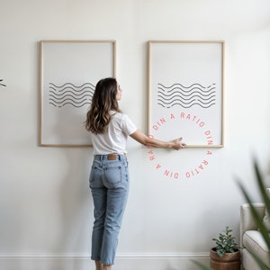 Può includere: Due stampe incorniciate con un designo di linee ondulate in bianco e nero. Le stampe sono appese a un muro bianco. Il testo "DIN A RATIO DIN A RATIO" è scritto in un cerchio attorno alle stampe.