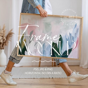 Puede incluir: Maqueta de marco rectangular de madera con una pintura abstracta en rosa, azul y verde. El marco lo sostiene una persona. El texto en el marco dice "Frame Mockup", "PSD, JPG & PNG" y "HORIZONTAL ISO DIN A RATIO".