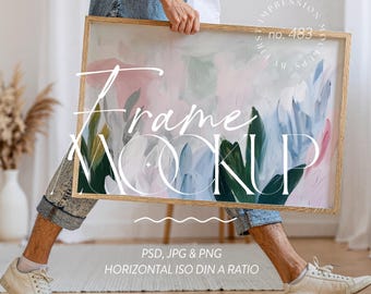 Puede incluir: Maqueta de marco rectangular de madera con una pintura abstracta en rosa, azul y verde. El marco lo sostiene una persona. El texto en el marco dice "Frame Mockup", "PSD, JPG & PNG" y "HORIZONTAL ISO DIN A RATIO".