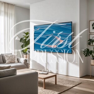 Puede incluir: Un interior de sala de estar con un televisor de pantalla plana grande montado en una pared blanca. El televisor muestra una imagen de paisaje azul y naranja. Un sof&aacute; gris con almohadas est&aacute; en primer plano. Una mesa de caf&eacute; de madera est&aacute; frente al sof&aacute;.