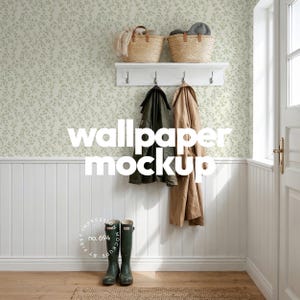 May include: A white wall with light green leaf-patterned wallpaper above white wainscoting. A white shelf holds two woven baskets. Below, a coat rack displays a dark green jacket and a tan coat. A pair of dark green rubber boots stands on the floor.