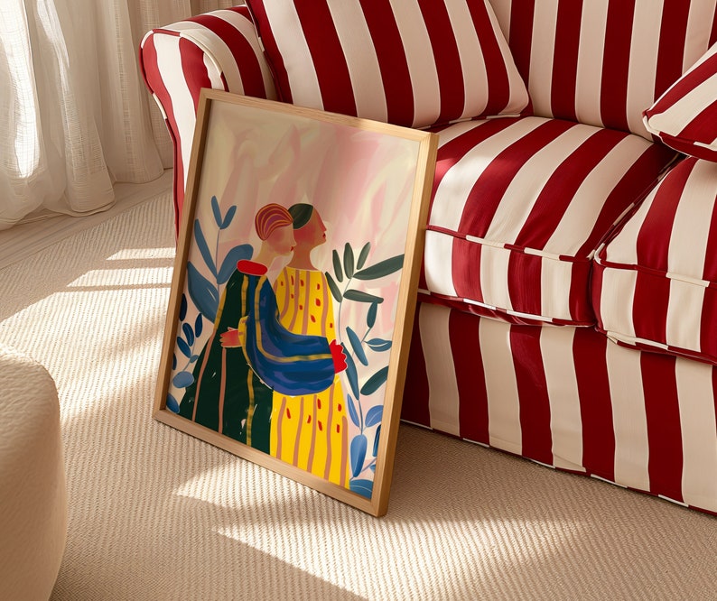 Puede incluir: Una impresi&oacute;n art&iacute;stica enmarcada que presenta dos figuras abraz&aacute;ndose, sobre un fondo de tonos rosas y azules. Las figuras est&aacute;n representadas con ropa colorida, una con un vestido a rayas amarillas y la otra con un atuendo verde y azul. La obra de arte est&aacute; rodeada de follaje verde.