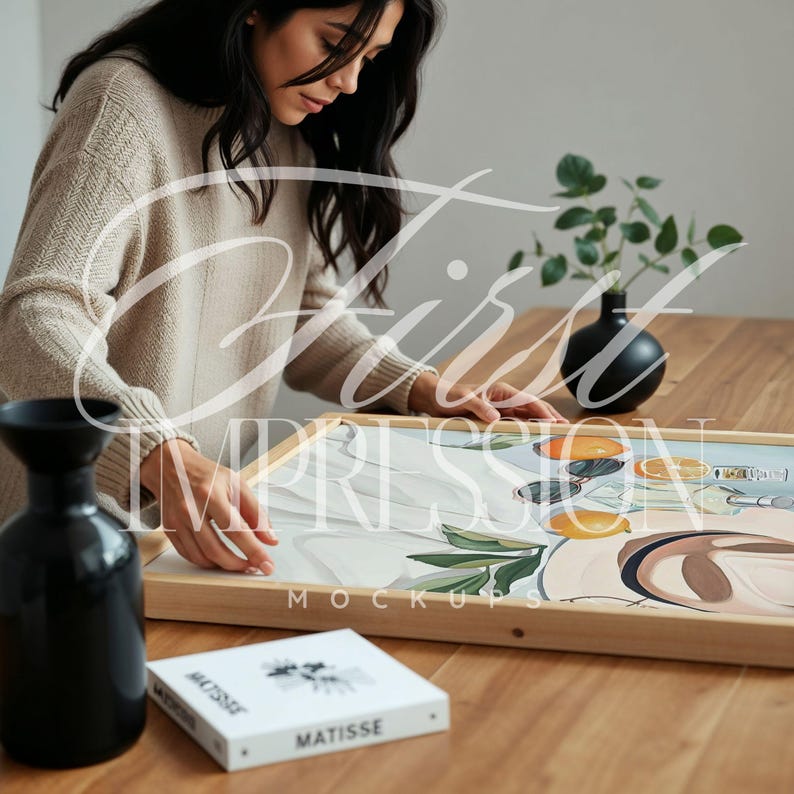 May include: A framed canvas print with a colorful abstract design featuring oranges, lemons, and leaves. The print is on a wooden table with a book and a vase.