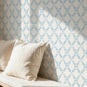 May include: A light-colored wall with a repeating blue floral pattern. Two off-white linen pillows rest on a bench. The wall is lit by sunlight, creating shadows.