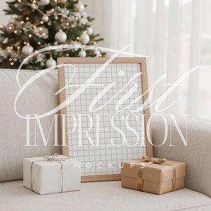 以下が含まれることがあります： 「First Impression Mockups」の文字が入った木製フレームのグリッドモックアップがベージュのソファに立てかけられています。白いギフトと茶色のギフトの2つがフレームの前にあります。背景には白いオーナメントのクリスマスツリーがあります。