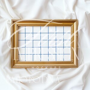 Puede incluir: Un marco de imagen de color dorado con un fondo blanco y un patr&oacute;n de cuadr&iacute;cula azul. El marco est&aacute; sobre una superficie de tela blanca.