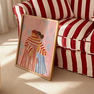 Puede incluir: Una impresi&oacute;n art&iacute;stica enmarcada que representa a dos figuras abraz&aacute;ndose, renderizada en un estilo suave y pict&oacute;rico. La obra de arte muestra figuras con ropa a rayas sobre un fondo rosa con acentos azul claro. El marco es de color madera clara.