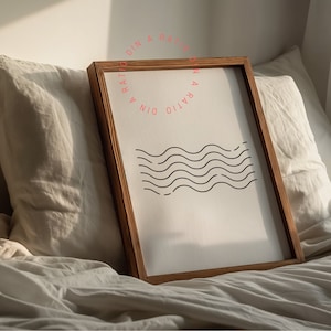May include: A framed print with a minimalist design of black wavy lines on a white background. The frame is made of natural wood and has a light brown finish. The print is titled "Din A Ration".