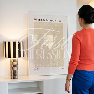 May include: A black and white striped table lamp with a geometric base sits next to a framed William Morris print. The print features a beige floral pattern and the text "Willow 1874". The lamp and print are on a white cabinet.