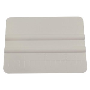 May include: White plastic squeegee with a rounded edge and a ruler marked 1, 2, and 3. The squeegee is used for applying vinyl decals and other adhesive materials.